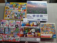 Four assorted 1000-piece puzzles in original boxes, showing various covers including retro collage, floral field, kitchen, and food-themed images.