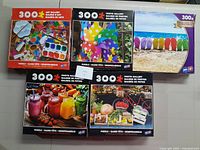 Lot of five 300-piece puzzles in their original boxes with colorful images visible on the packaging