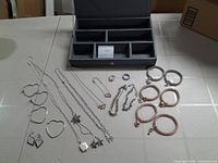 Photo showing assortment of jewelry including open box, heart-shaped earrings, several bracelets, a couple of rings, and necklaces with varied pendants and chains.