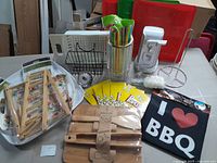Photo showing assorted kitchen items including bamboo serving set tied with rope, floral ceramic tray, wooden trays, container with colorful straws, tall white electric can opener, metal tiered dish rack, and boxed popcorn bags.