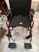 Front view showing black nylon seat with some wear on the fabric, removable foot supports, and sturdy red metal frame.