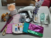 Full lot view showing a Conair hair dryer, scalp massager, nail stickers, hairbrushes, massage tool, and multiple makeup bags on a table.