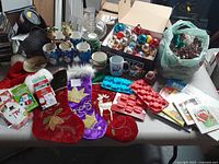 Photo showing assortment of Christmas decorations including three stockings, several Christmas mugs, box of assorted ornaments, silicone molds, books, card games, and craft supplies in a green bag.