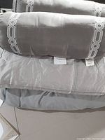 Close-up photo showing the grey comforter fabric and matching embroidered roll pillow on top