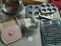 Metal muffin and tart pans, roasting pan, cooking racks, bacon trays, steamer pot with lid, convection microwave cookware and rack, all arranged on a table.