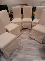 Six cream upholstered dining chairs arranged in a semicircle, showing overall condition and fabric skirts.