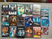 Photo showing a collection of 18 DVD and Blu-ray cases arranged in rows on a gray surface