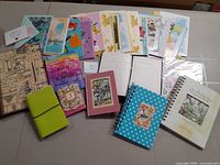 Photo showing all the greeting cards and notebooks laid out on a surface including vintage and floral motifs notebooks, motivational cards, and animal-themed greeting cards