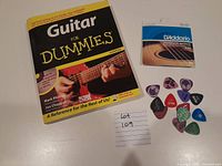 'Guitar For Dummies' book, package of guitar strings, and assorted picks laid out flat