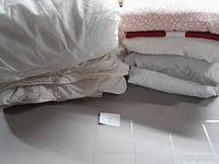 Photo shows stacked white and cream colored duvets and bedding linens