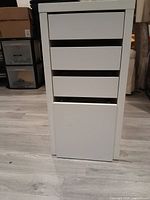 Front view of white 4-drawer filing cabinet showing drawer fronts and bottom drawer with hanging folder rack.
