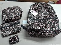 Floral backpack with two medium/small bags and one small Airpod case shown on a white surface showing front and side views, black background with pink and white small flowers.