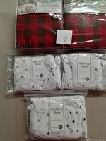 Photo showing the two red and black lumberjack/checkered crib sheets and three white mini crib sheets with arrow prints, all new and in package.