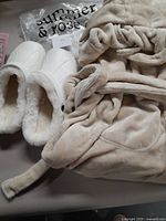 General view showing beige plush robe and white slippers with packaging