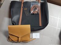 Overview of the black tote bag with brown handles, showing the yellow tech accessory pouch placed in front and the handbag surface.