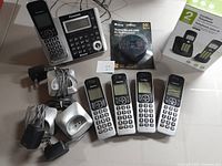Wide shot showing Panasonic phone system with base unit, four cordless handsets, three charging bases, extra Panasonic cordless phone, new V-Tech phone boxed, and telephone line cord.