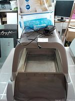 Full view of the automatic litter box with reusable metal tray inside and power adapter placed on top.