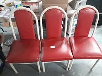 Three red vinyl upholstered chairs with white metal tubular frames, arranged side by side.