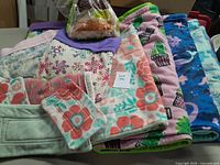 Photo of assorted folded fleece bedding pads with floral, snowflake, and animal prints in multiple pastel colors