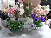Overall view of artificial flowers and vases on table with various colors and arrangements.