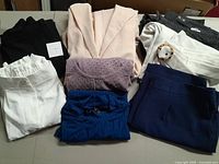 White dress shorts, light pink blazer, purple sweater, navy pants, dark gray and black pants, black and white shirts visible together on table.