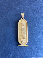 Front view of gold cartouche pendant showing hieroglyphic design