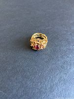 Top view of ornate ring on black background showing red stones and filigree