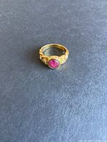 Top-down view of the gold ring showing central cabochon and accent stones on grey background