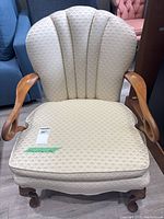 Front view of antique upholstered armchair with beige diamond patterned fabric, curved wooden arms and cushion.