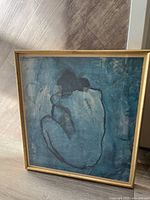 Full view of the first framed abstract art piece with blue background and black figure under glass