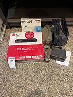 Photo showing LG Blu-ray Disc/DVD Player in box, Philips Travel Iron box, and clock radio with power cord