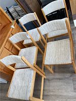 Five chairs positioned together highlighting their natural wood frames and light fabric upholstery with visible wear and stains.