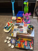 Full overview of lot including Fisher Price toys, wooden blocks, Lego box, tea set cups and saucers, toy golf clubs and more.