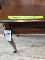 Close-up photo showing the carved curved leg and a hanging sale tag, highlighting the wood structure and finish.