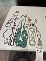 Wide view of all costume jewelry pieces arranged on a white table showing several necklaces, bracelets, earrings, and pins.