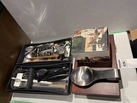 Two trays containing various cutlery and kitchen utensils, a metal spoon rest and a boxed automatic stirrer