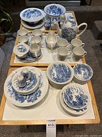 Full view of dinnerware set showing teapot, cream and sugar containers, salt and pepper shakers, cups, bowls, plates on trays.