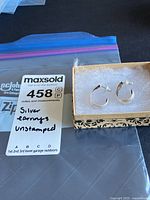 Pair of hammered silver hoop earrings in small decorative box next to auction tag labeled 'Silver earrings unstamped'