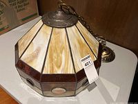 Side angle view of stained glass hanging light fixture showing amber and cream swirled glass panels with dark metal top and chain.