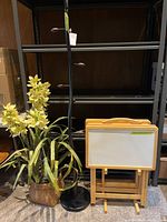Photo showing the coat rack, faux plant, and set of four wooden framed whiteboard TV trays on a folding stand in front of shelving unit.