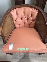 Front view of mid-century barrel chair showing tufted pinkish-peach upholstered backrest, cane sides, and removable seat cushion with dimensions written on tape.