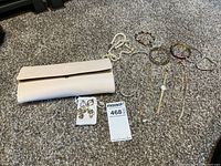 Photo showing white leather Pandora jewelry travel wallet with various costume jewelry items including bracelets, earrings, watch, and necklaces laid out on carpet.