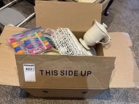 Box with assorted kitchen items including plastic containers, clips, insulated gravy server, and wire rack.