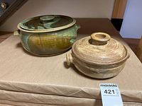 Photo of two pottery bowls with lids on a brown paper-covered surface, showing one green/brown glazed bowl and one tan bowl.