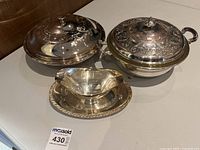 Photo showing two large silver covered serving dishes and one silver gravy boat with underplate, all with ornate designs.