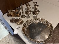 Overview photo showing silver plated scalloped serving platter, multiple candle holders, cream and sugar set on tray, and coasters.