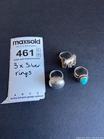 Photo of the three silver rings arranged on a black background with auction tag.