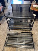 Simplehuman duo garbage bin stainless steel with two black metal shoe racks on carpeted floor, showing whole lot as arranged together