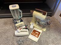 Three vintage kitchen appliances on carpet: Sunbeam Mixmaster stand mixer with glass bowl and two beaters, Sunbeam hand mixer, and Osterizer Pulse Matic blender with glass pitcher and buttons.