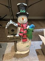 Full view of snowman figure showing details of hat, scarf, birdhouse, and stocking gifts